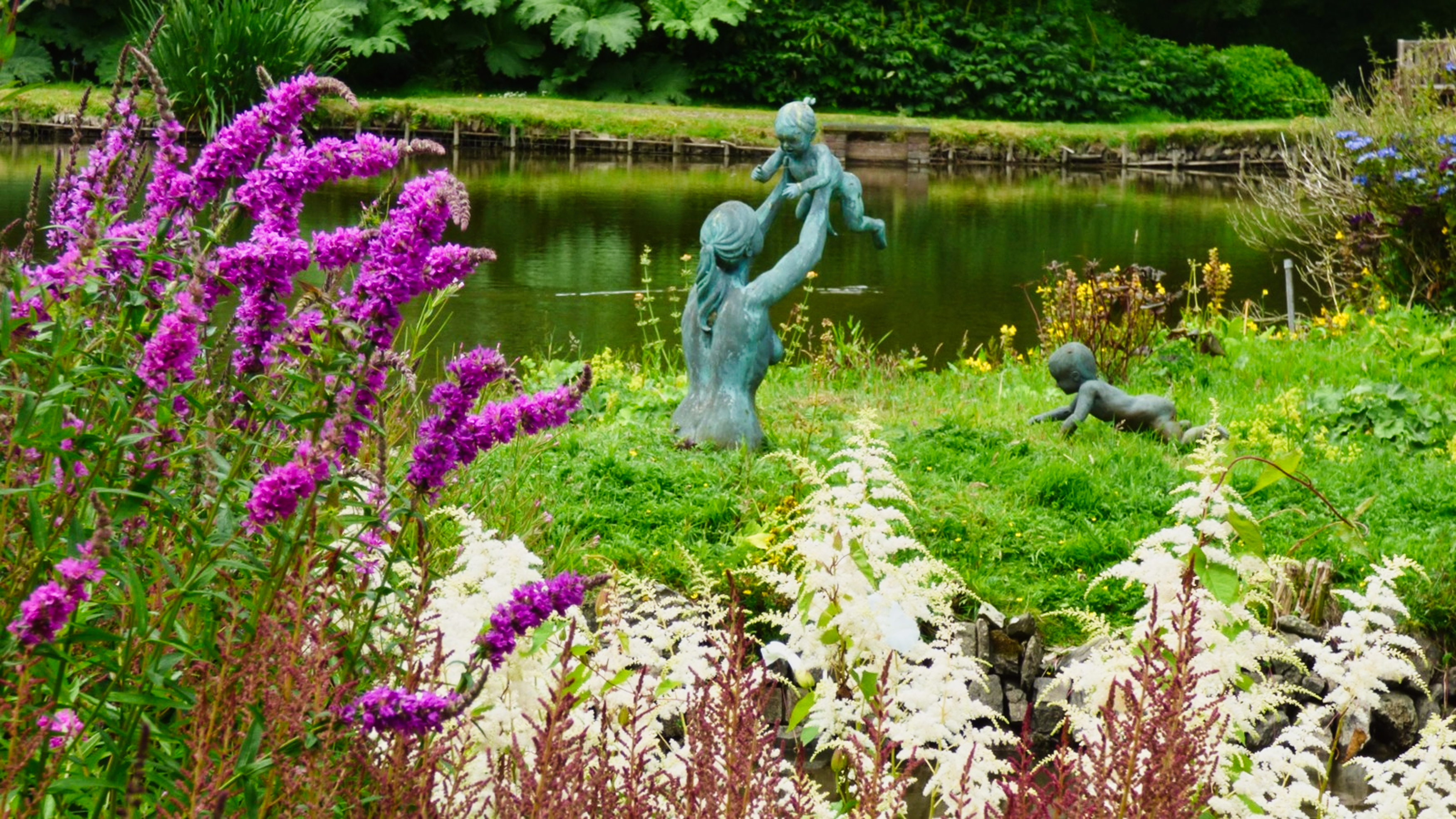 Photo of a statue next to a lake and flowers