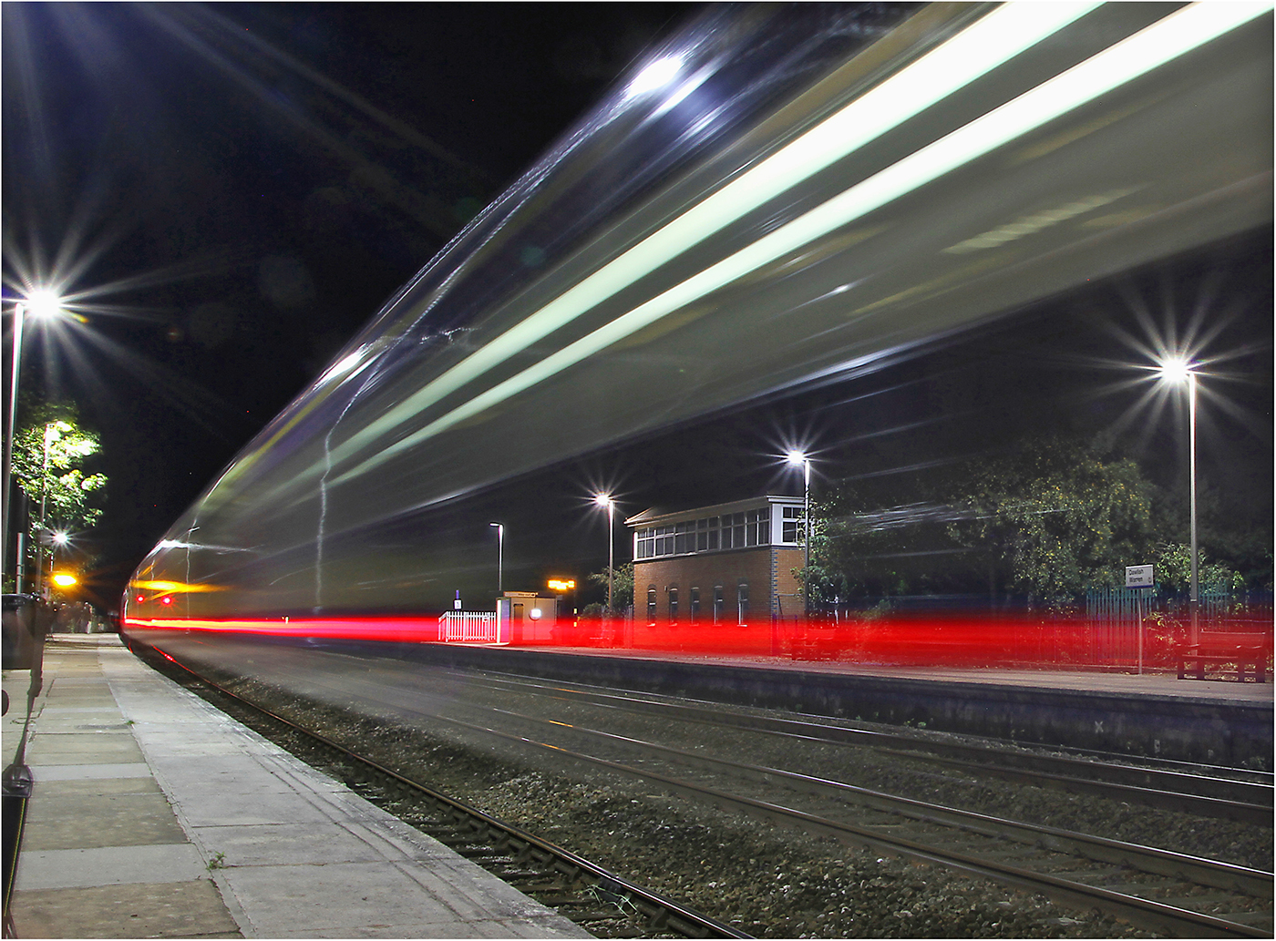 A photo of a train moving through a station at night.