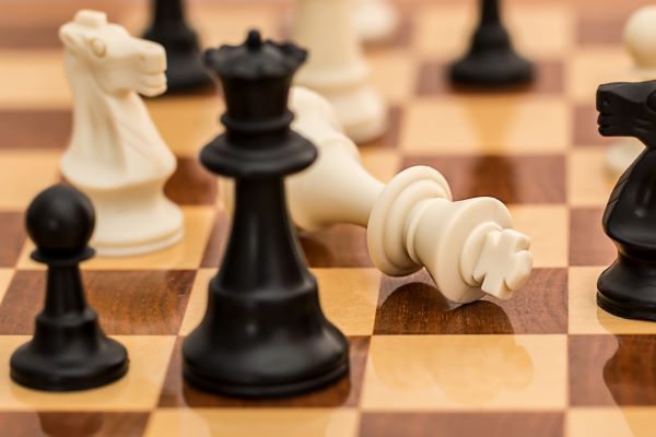Chess pieces on a brown squared board, a white piece has been knocked over