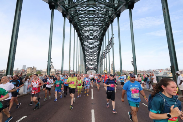 runners run towards the camera across a tall iron bridge