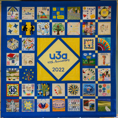 A quilt with forty square blocks and in the middle a yellow square and the words u3a 40th Anniversary 2022