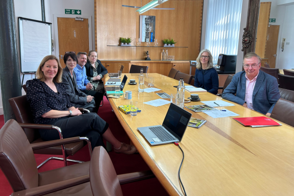 Francois Vellas meeting with members of u3a office - they are sitting round a desk in a meeting room with laptops, notebooks and pieces of paper on the table