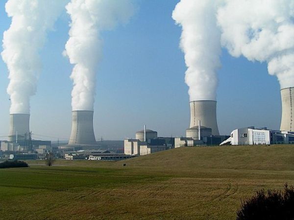 nuclear power plant with plumes of white smoke against blue sky 